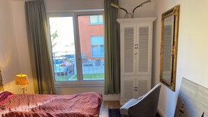 A hotel room with a bed, a chair, a wardrobe, a mirror, and a window with a view of the outside. - Ketzin Havel modern apartment with private garden, close to the water (ketzin)