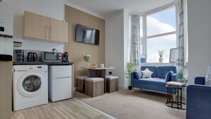 Un espacio habitable compacto con kitchenette, lavadora, TV de pantalla plana, sofá azul y comedor.