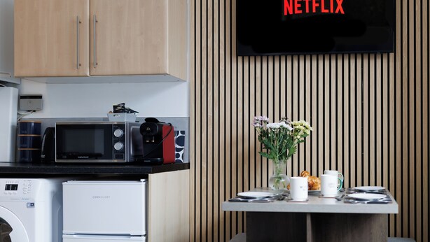 Una cocina moderna con armarios de madera, un microondas, una cafetera y una mesa con un florero y tazas.