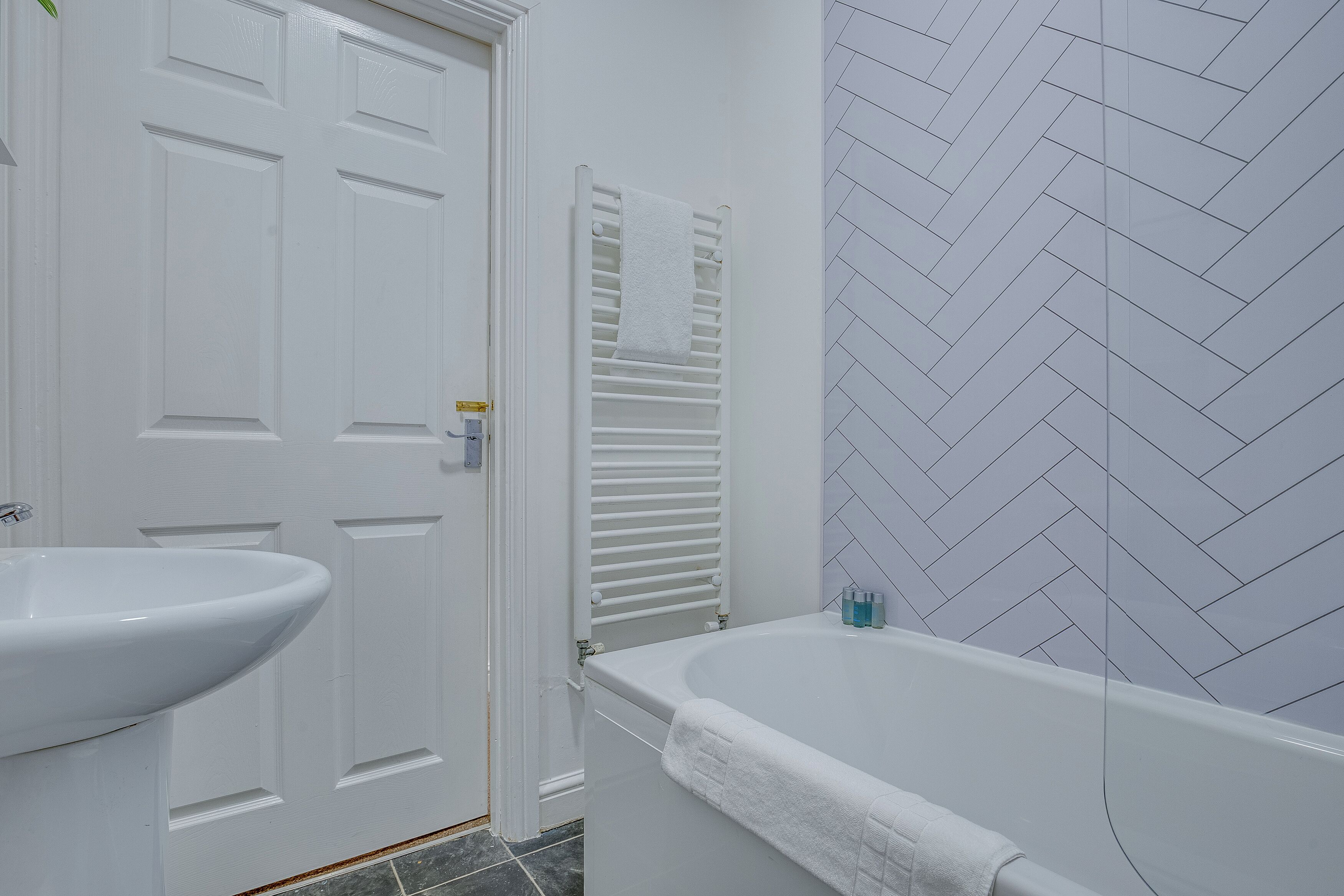 Un baño con lavamanos blanco, bañera y barra para toallas.