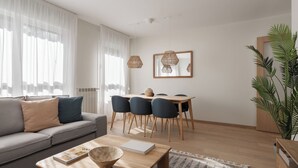 A modern living room with a sofa, coffee table, dining table with chairs, and a large plant.