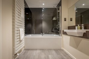 Een moderne badkamer met een ruime badkuip, een douche met glazen wanden en een wastafel met spiegel.