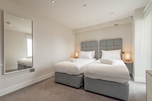 Een moderne slaapkamer met twee bedden, een grote spiegel en bedlampjes.