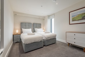 Une chambre avec deux lits, une table de chevet, une commode et un tableau encadré au mur.