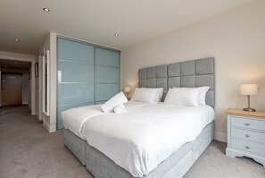 A bedroom with a large bed, a grey headboard, a bedside table with a lamp, and a blue sliding door. - Square Green (No 13) | Balcony (St Andrews)