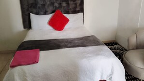 A neatly made bed with a white duvet, a red pillow, and a grey blanket. - 0688429688 Guesthouse in Mafikeng  (Mahikeng)