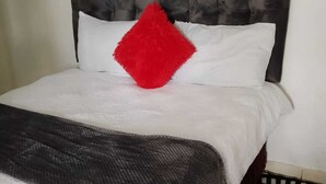 A bed with a tufted headboard, white bedding, a red pillow, and a patterned throw. - 0688429688 Guesthouse in Mafikeng  (Mahikeng)