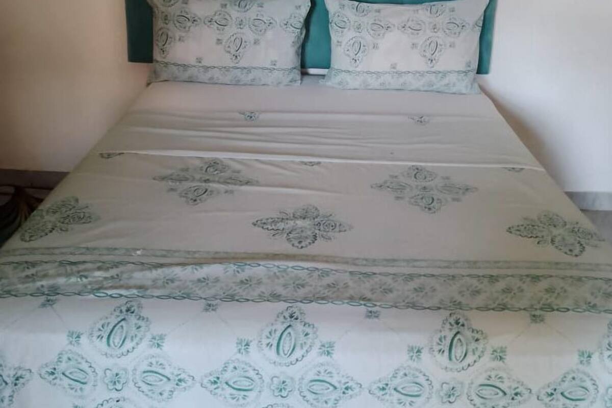 Ein Bett mit einem türkisblauen Kopfteil und gemusterten Bettwaren.