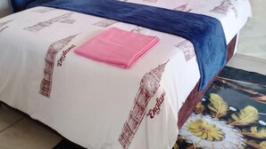 A bed with a red headboard, white bedding with 'England' printed on it, a blue chair, and a pink towel on the bed. - 0688429688 Guesthouse in Mafikeng  (Mahikeng)