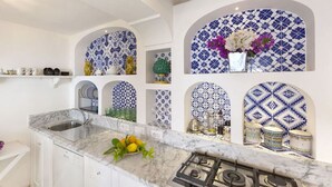 Une cuisine avec des meubles blancs, un plan de travail en marbre et des carreaux bleus et blancs formant un motif sur les murs.