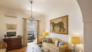 A living room with a sofa, a television, a wooden cabinet, a dining table, and a view through a glass door.