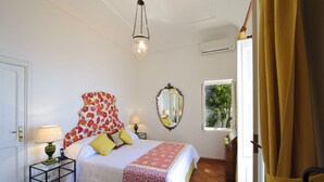 A bedroom with a bed, bedside table, lamp, mirror, and window with curtains.