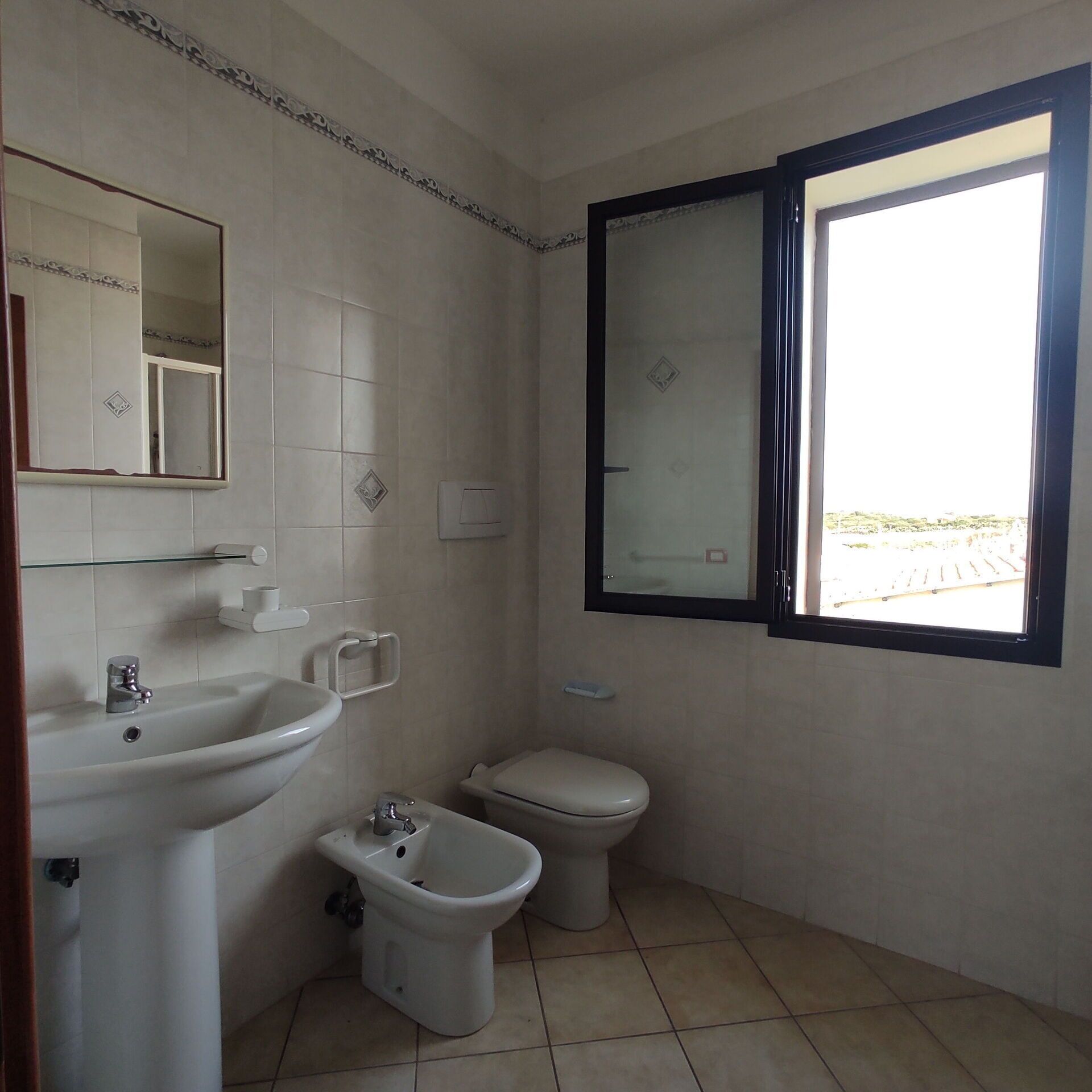 Une petite salle de bain avec un lavabo, des toilettes et un bidet. Il y a une fenêtre donnant sur l’extérieur.
