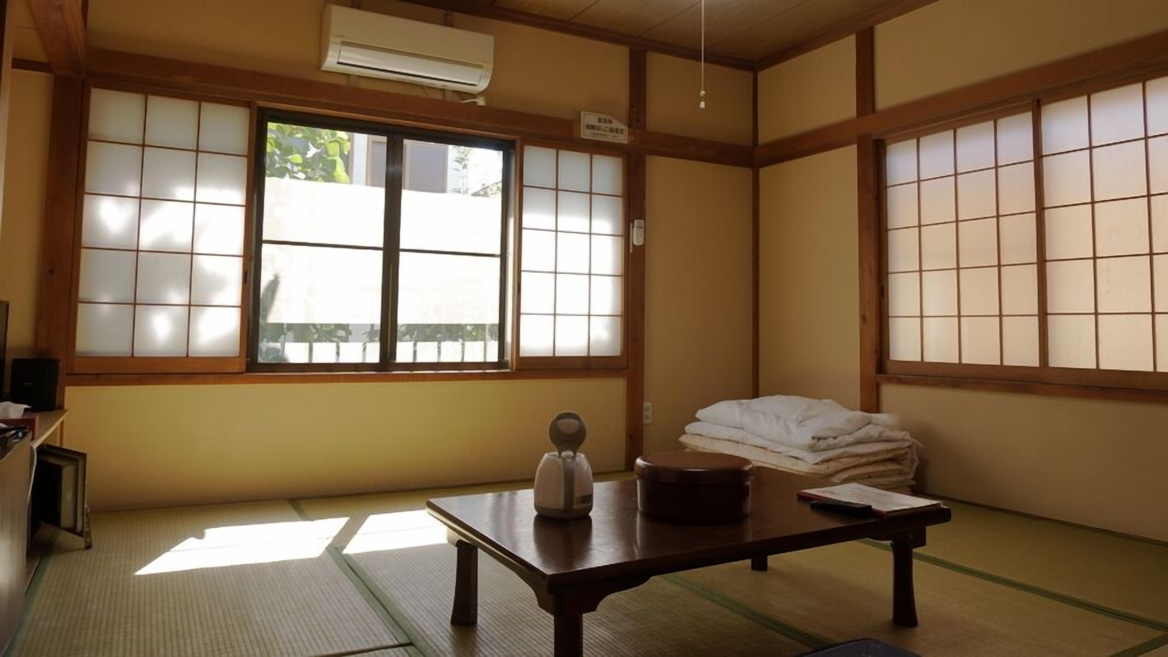 Een traditionele Japanse kamer met tatami vloeren, een lage tafel met een waterkoker en een boek, en een raam met verschuifbare shoji deuren.