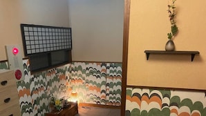 Una habitación con un papel tapiz estampado, una mesita con una lámpara y una estantería con una planta.