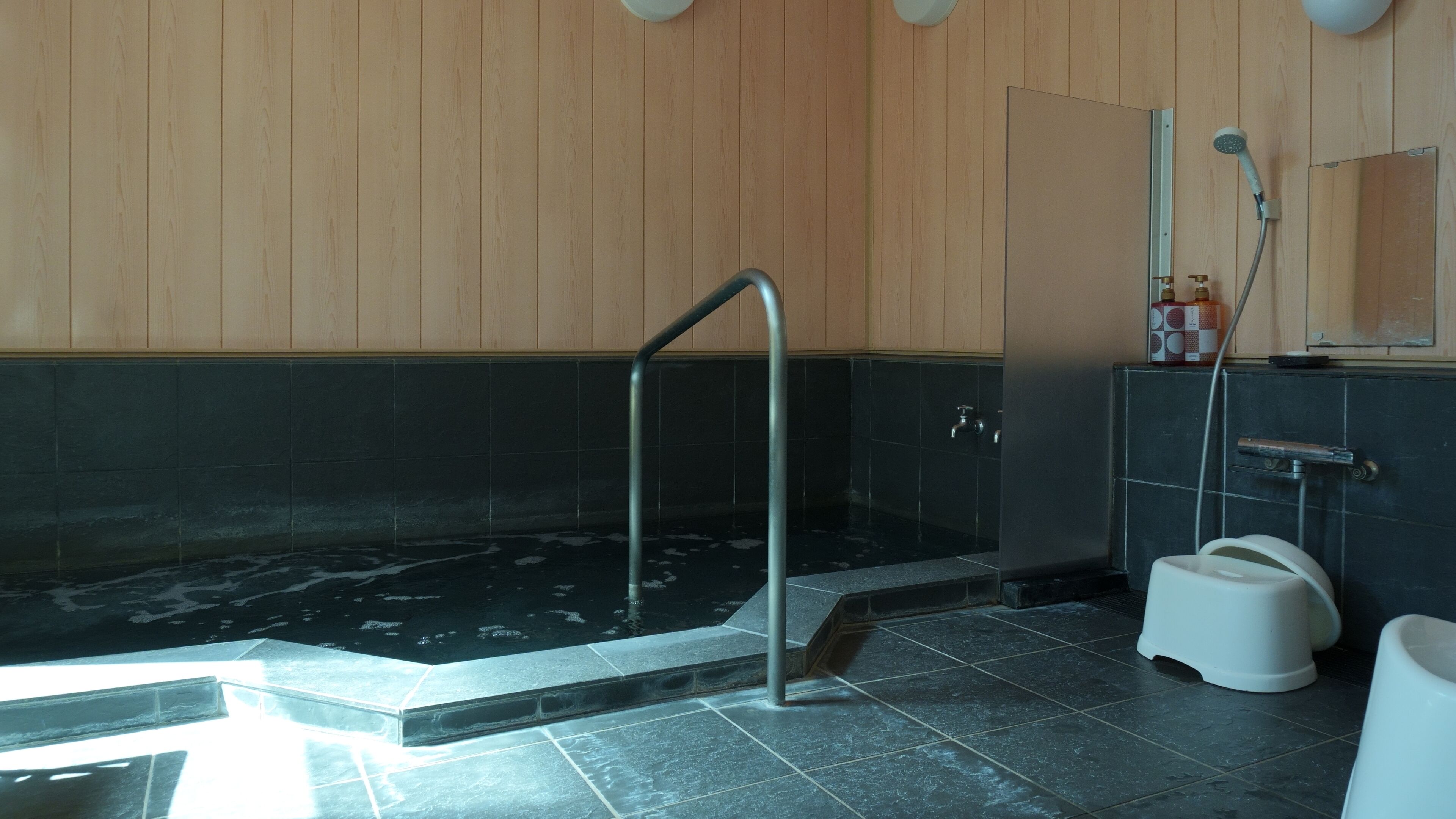 Un bagno moderno con parete in legno, una vasca da bagno nera, un WC bianco e uno spazio doccia.