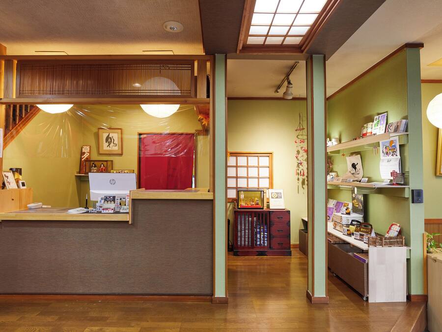 Una zona de recepción con mostrador de madera, una cortina roja y un estante en la pared con diversos objetos.