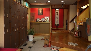 Un interior japonés tradicional con taquillas de madera, una pared roja con caligrafía y suelo de madera.