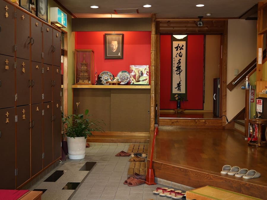 A traditional Japanese interior with wooden lockers, a red wall with calligraphy, and a wooden floor.