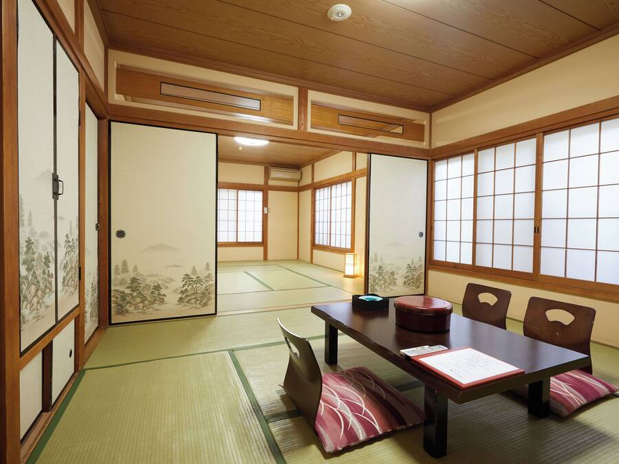 A traditional Japanese room with tatami flooring, shoji screens, and a low wooden table with cushions.