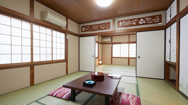Una habitación japonesa tradicional con suelo de tatami, puertas correderas y una mesa baja con cojines.