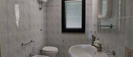 Un baño con dos inodoros, un lavamanos y una ventana.