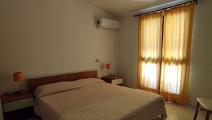 Camera d'albergo standard con un letto singolo, comodini con lampade, una finestra con tende e un condizionatore d'aria a parete.