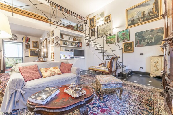 A spacious living room with a high ceiling, a staircase, and a variety of artworks and decorative items.