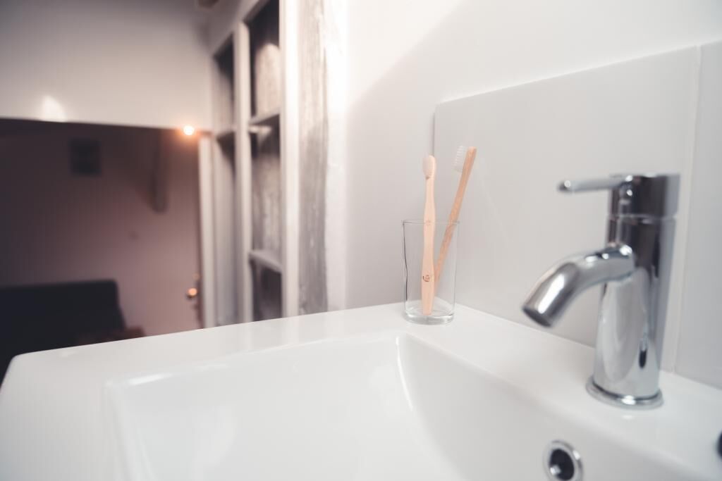 Ein Badezimmerwaschbecken mit Armatur aus Chrom und zwei Zahnbürsten in einem Glas.