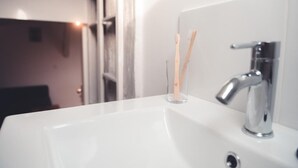 Un lavamanos con grifo cromado y dos cepillos de dientes en un vaso transparente.