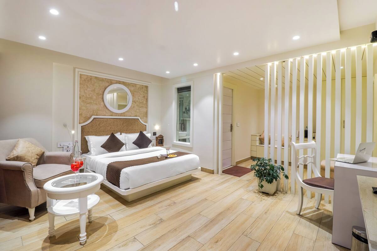 A modern hotel room with a bed, a chair, a small table, and a desk with a laptop.
