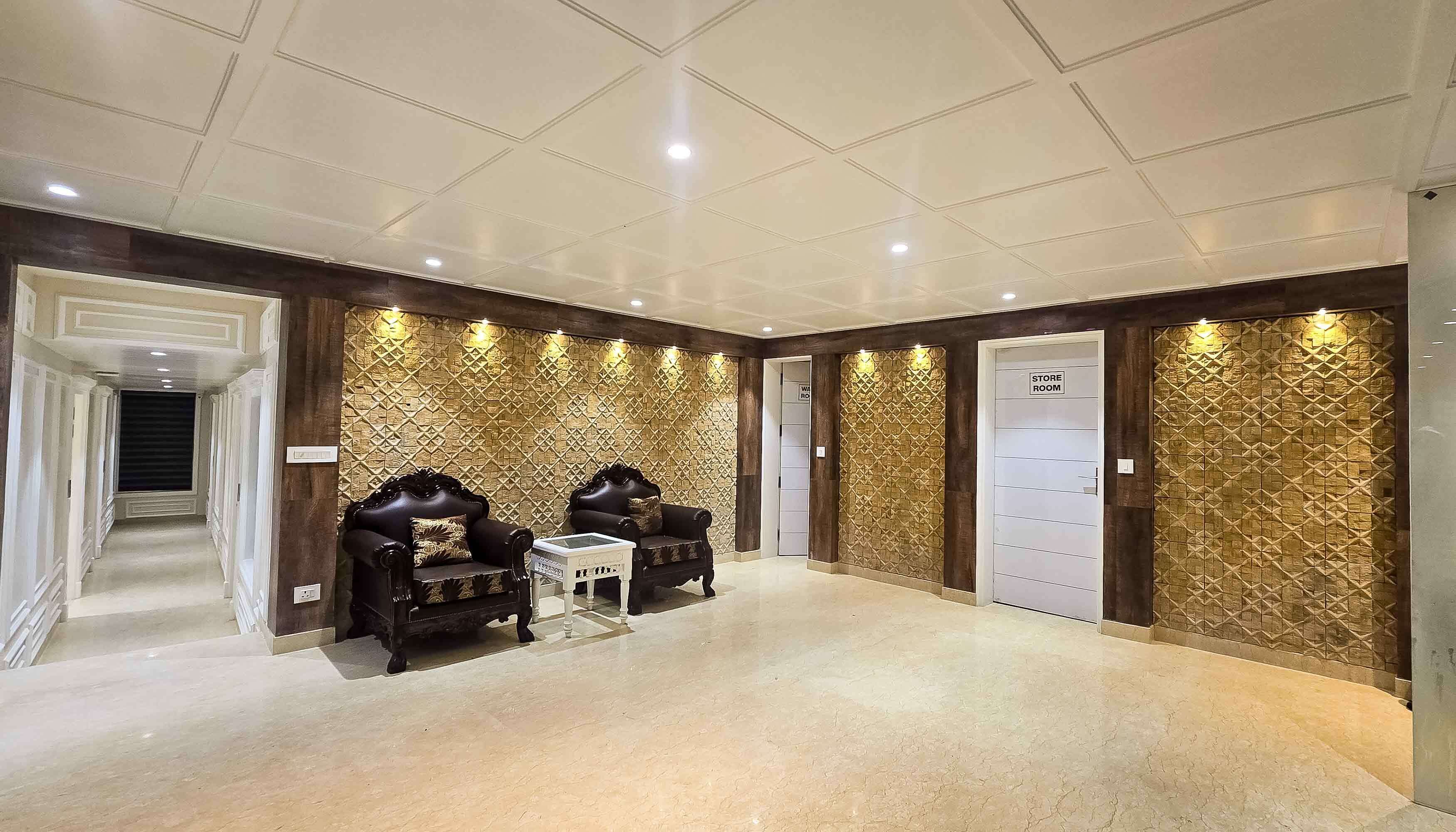 Una habitación amplia con dos sillones marrones oscuros, una mesita blanca y una pared con diseño geométrico. Se observa una puerta con la etiqueta “STORE ROOM” y un cartel que indica “WATER ROOMS” en la pared.