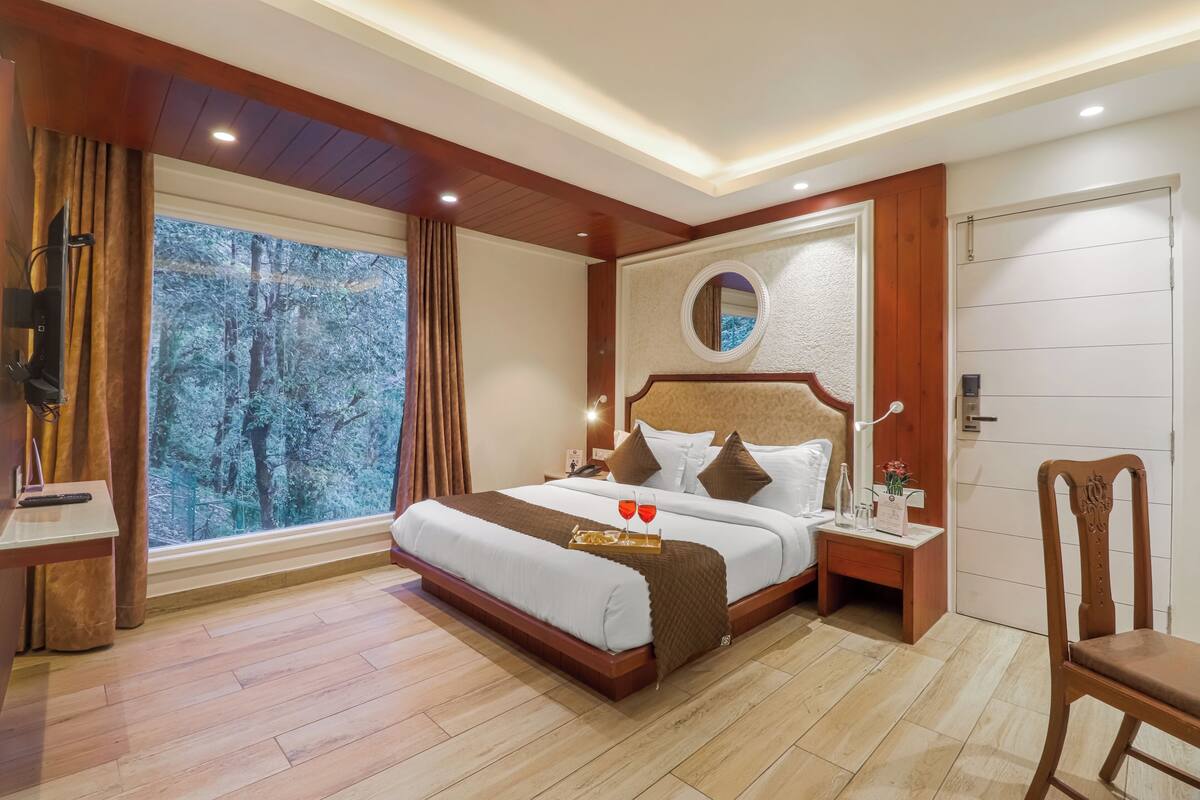 A bedroom with a large bed, bedside tables, a mirror, and a view of trees through the window.