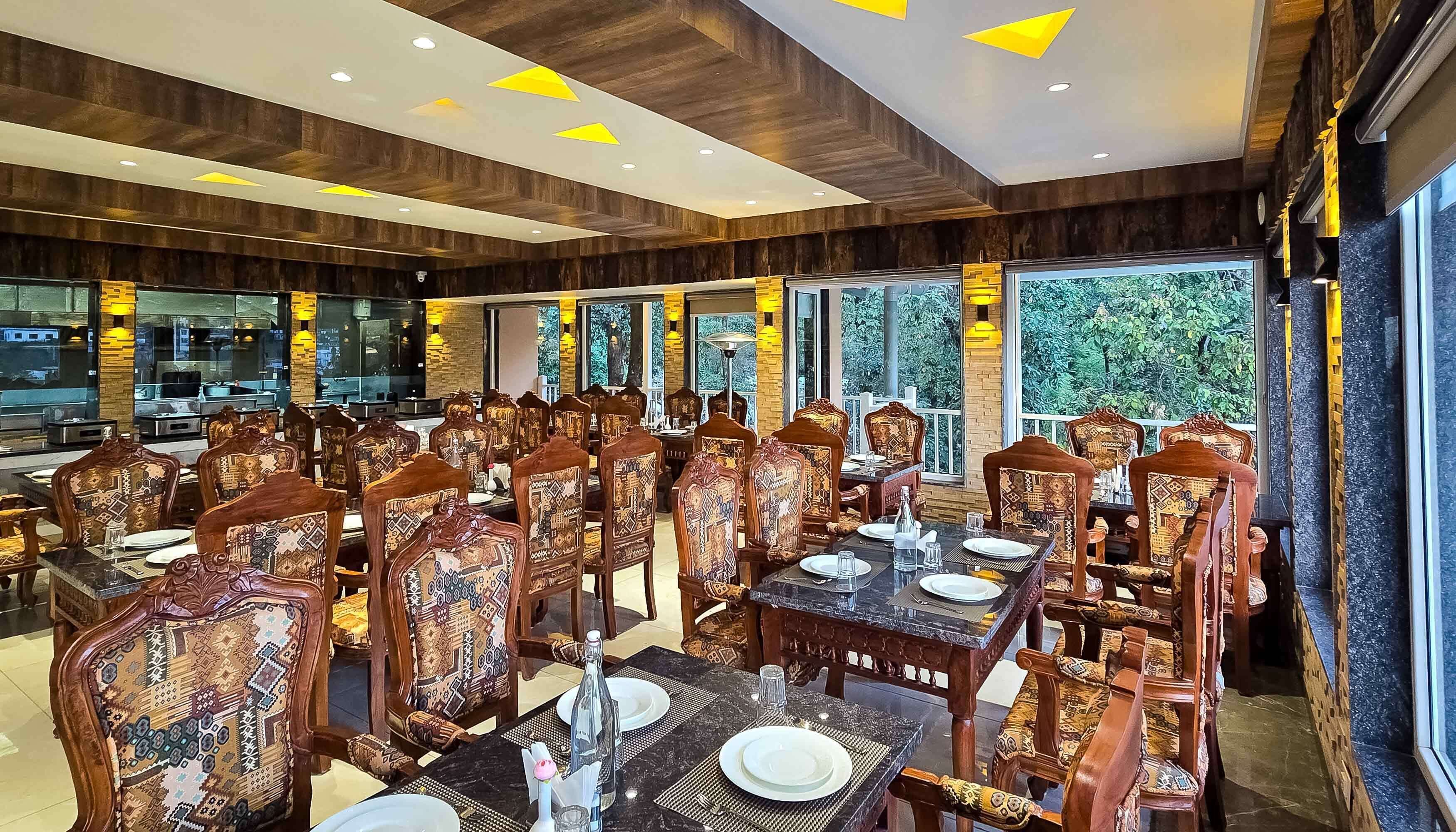 A restaurant with wooden paneling, patterned chairs, and large windows offering a view of greenery.