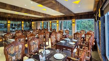 A restaurant with wooden paneling, patterned chairs, and large windows offering a view of greenery.