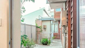 A narrow pathway leading to a building with a wooden exterior and a metal railing. There are potted plants and a doormat at the entrance. - Ellen Fremantle City Centre - Walk everywhere. Secure free parking. (Fremantle)