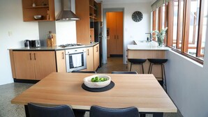 A modern kitchen with wooden cabinets, a gas stove, and a dining area with a table and chairs. - Ellen Fremantle City Centre - Walk everywhere. Secure free parking. (Fremantle)