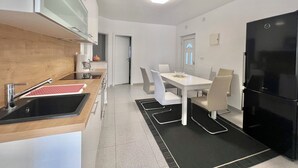 Een moderne keuken met een zwarte koelkast, witte kastjes en een houten aanrecht. Er is een eethoek met een witte tafel en stoelen.