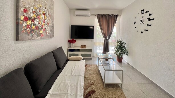 Een moderne woonkamer met een bank, een flatscreen televisie, een decoratief schilderij, een klok en een potplant.