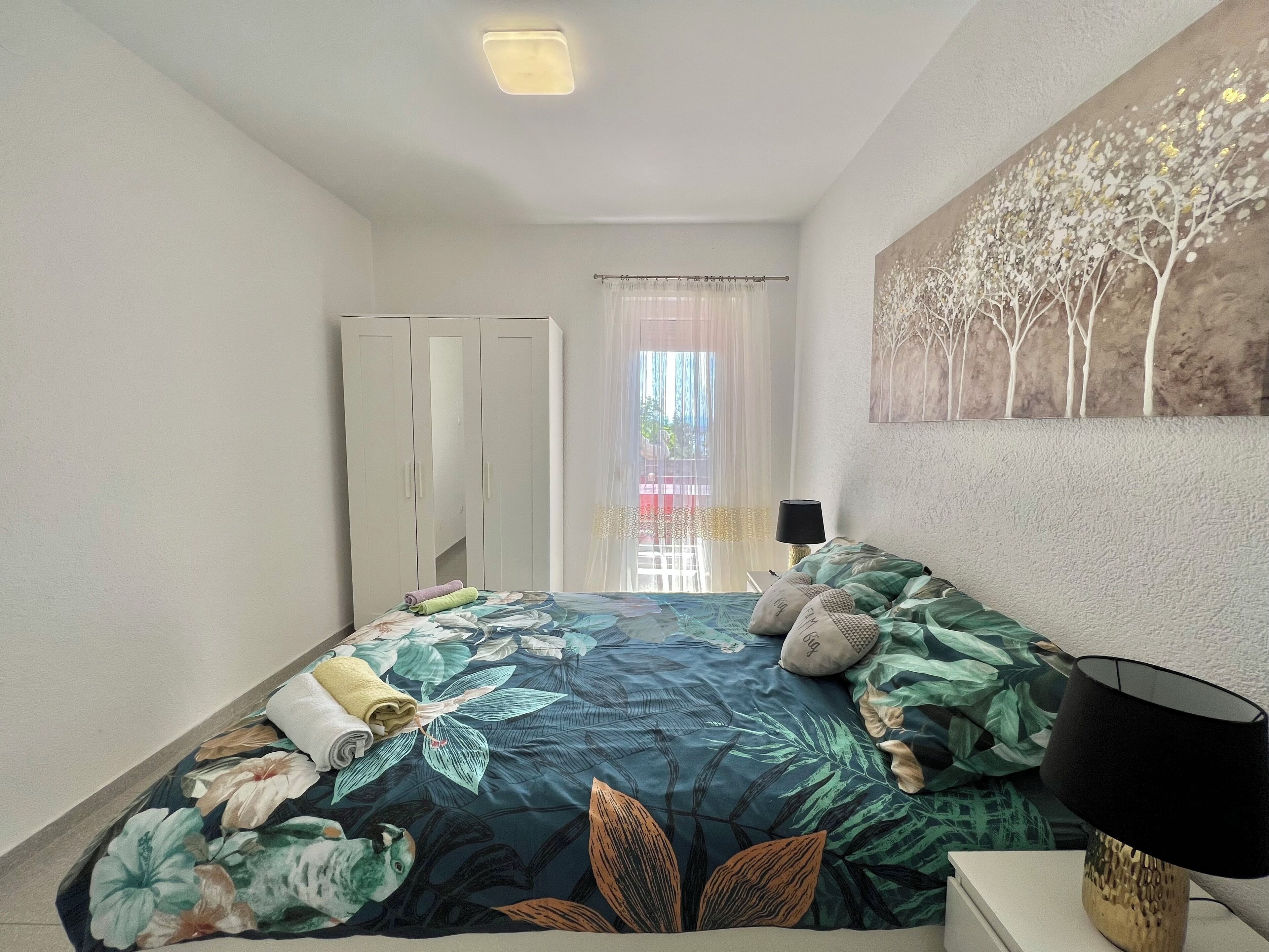 Una camera da letto con un letto, un armadio, un quadro e una finestra con tende.