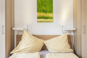 Una cama con dos almohadas, cabecera e imagen colgada en la pared de un campo.