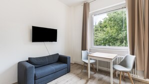Una sala de estar moderna con un televisor de pantalla plana montado en la pared, un sofá gris, una mesita de madera, dos sillas y una ventana con cortinas.