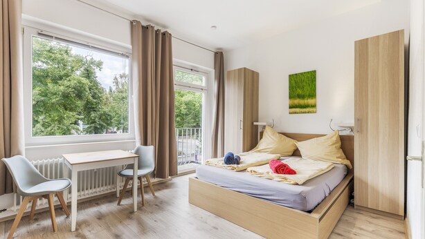 Un dormitorio con cama, escritorio, silla y vistas a árboles desde la ventana.