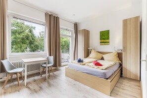 Une chambre à coucher avec un lit, un bureau, une chaise et une vue sur les arbres par la fenêtre.
