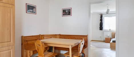 Un rincón comedor con mobiliario de madera, dos cuadros enmarcados en la pared y vistas a otra habitación con un radiador y una ventana.