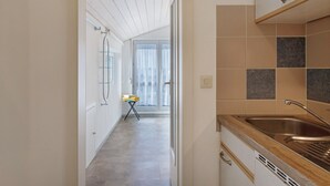 Eine schmale Küche mit Holzarbeitsplatte, Spüle aus Edelstahl und einem Fenster mit Vorhängen.