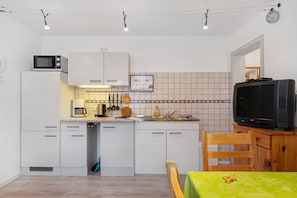 Una cocina compacta con armarios blancos, un microondas, una cafetera y un televisor sobre un soporte de madera.