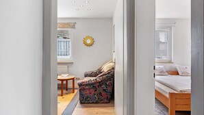 A narrow hallway leading to a living area with a sofa, a small table, and a bed with a window. - Apartment 'Belchen, 59qm' with Wi-Fi (Schönwald im Schwarzwald)