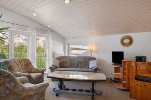 A room with a sofa, armchairs, a coffee table, a TV, and a sunburst wall decoration.
