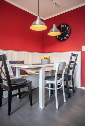 Un coin repas avec une table blanche, des chaises noires et blanches, des murs rouges et une horloge.